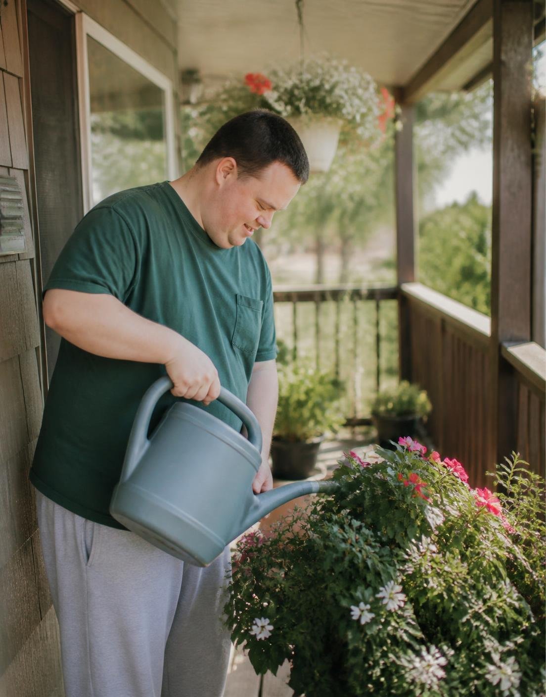 An adult watering potted plants on a sunlit front porch
